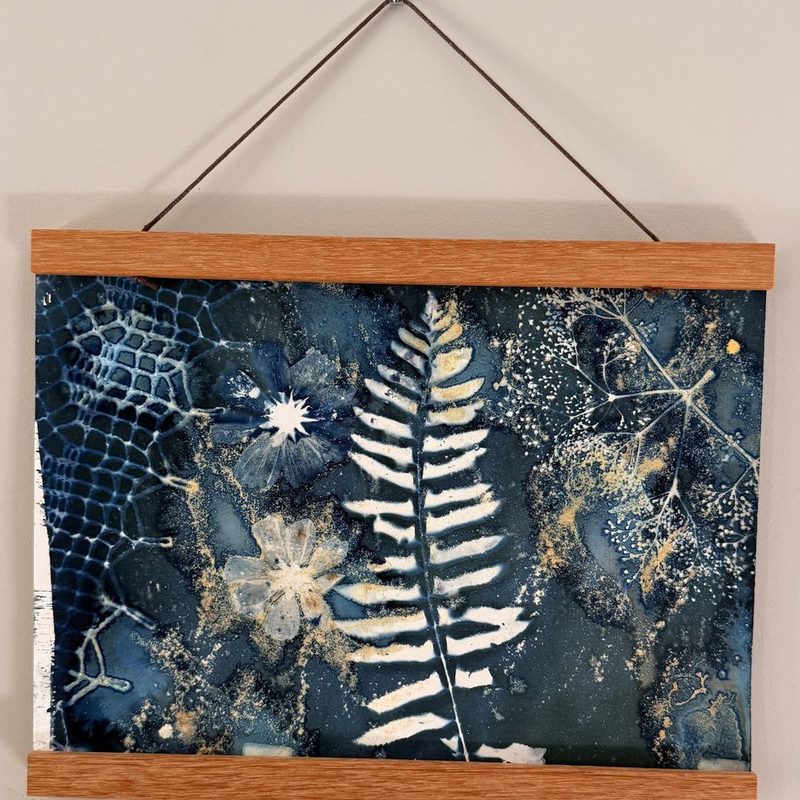 Bonus 3: a framed wet cyanotype hanging on the wall, dark mottled blue with a white fern and flecks of gold from turmeric